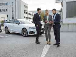 Zwei Männer und eine Frau beraten sich. Dahinter steht ein weißer Audi.